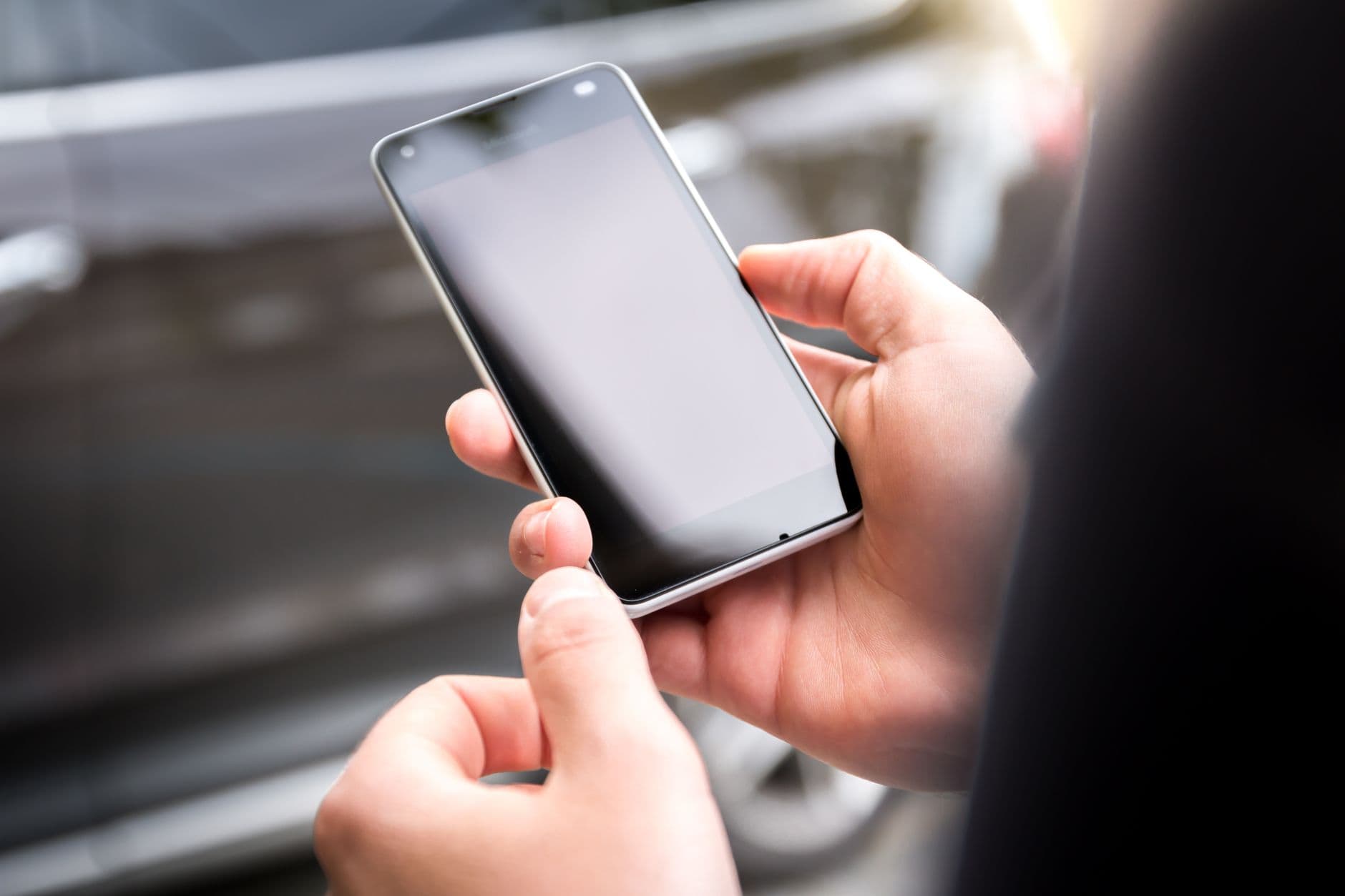 Manos consultando la pantalla de un telefono movil en la calle