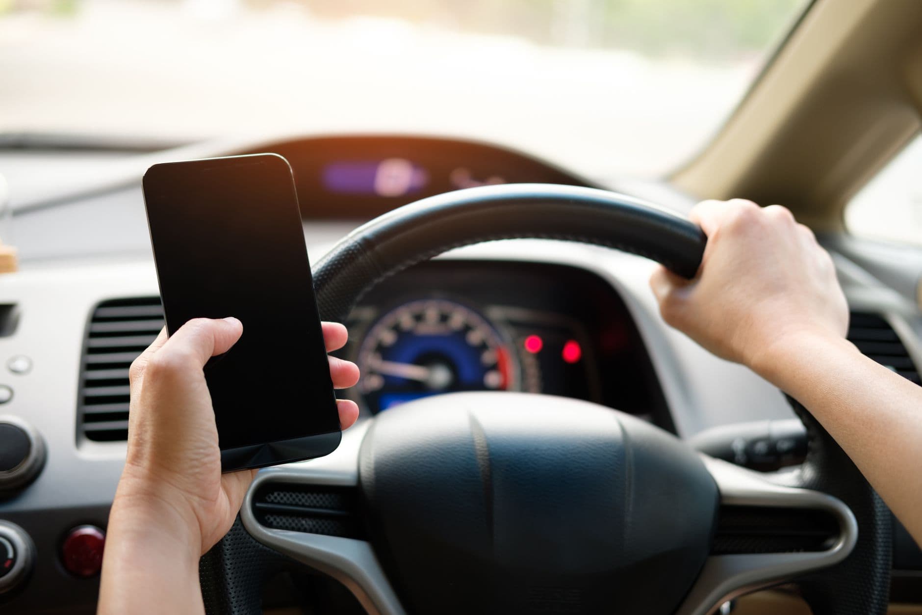 Persona sujetando el movil con una mano y el volante con la otra