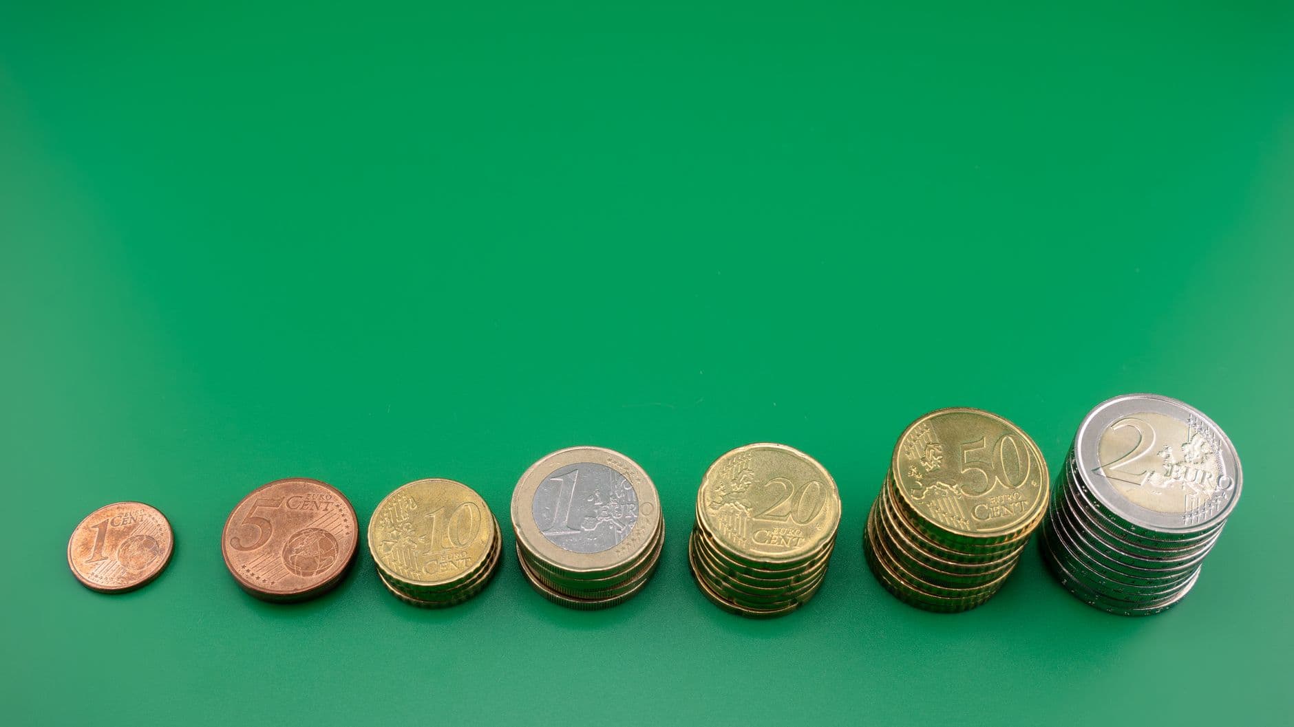 Montones de monedas de euro ordenados de menor a mayor sobre un fondo verde